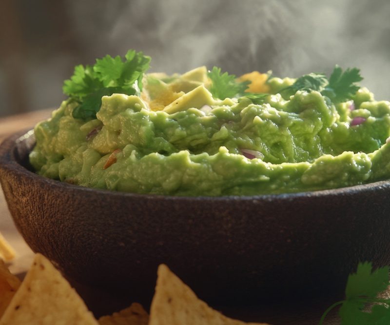 Bowl of creamy guacamole and crunchy chips on cutting board, perfect for snack time or party